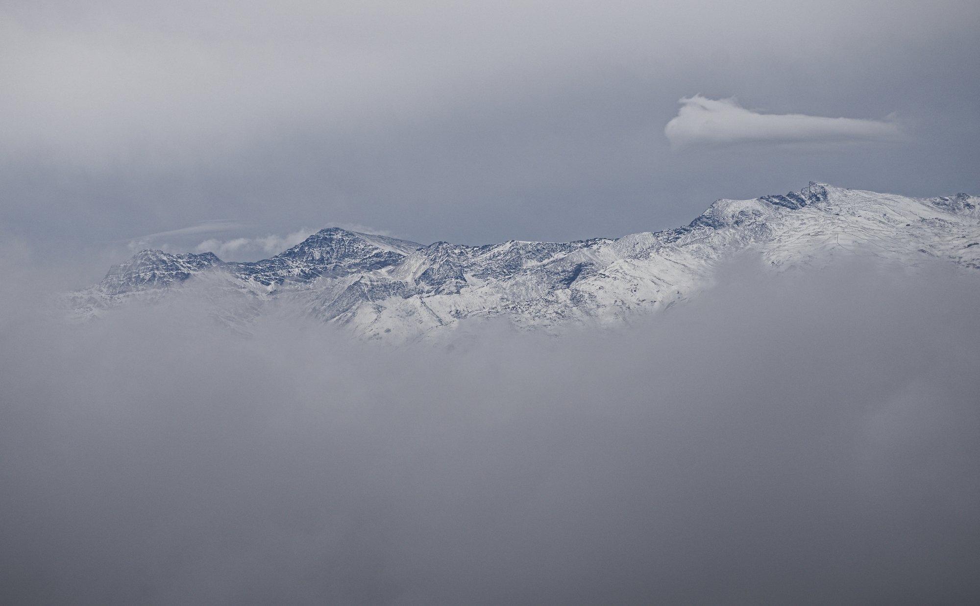 A view of snowy mountains thought an opening in the clouds. Show's the three highest peaks of Spain's Sierra Nevada. On the left Alcazaba (3371m). In the middle Mulhacen (3482m). On the far right Veleta (3394m)