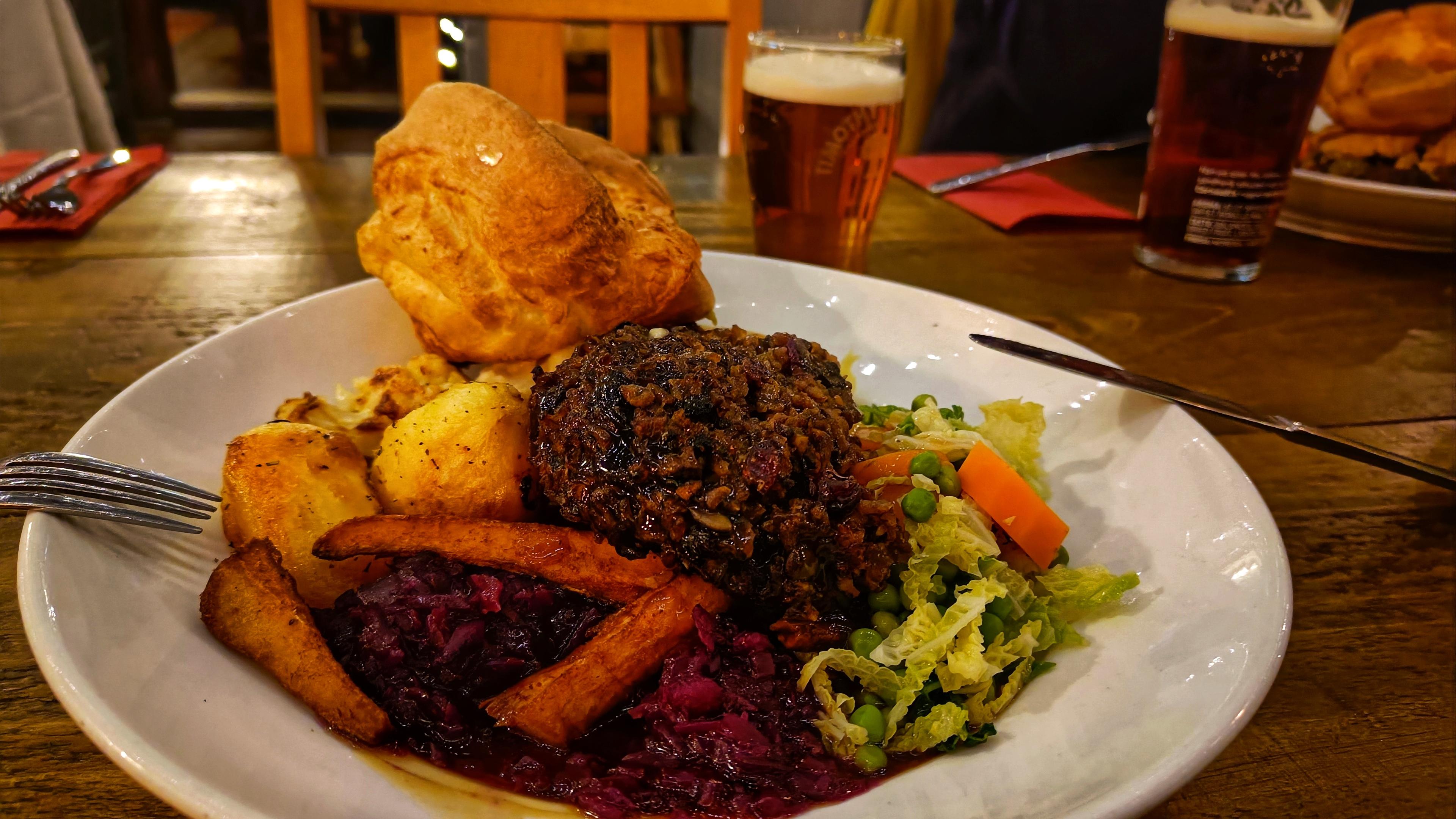Picture of a Sunday roast dinner on a white plate. Half a pint of beer behind.
