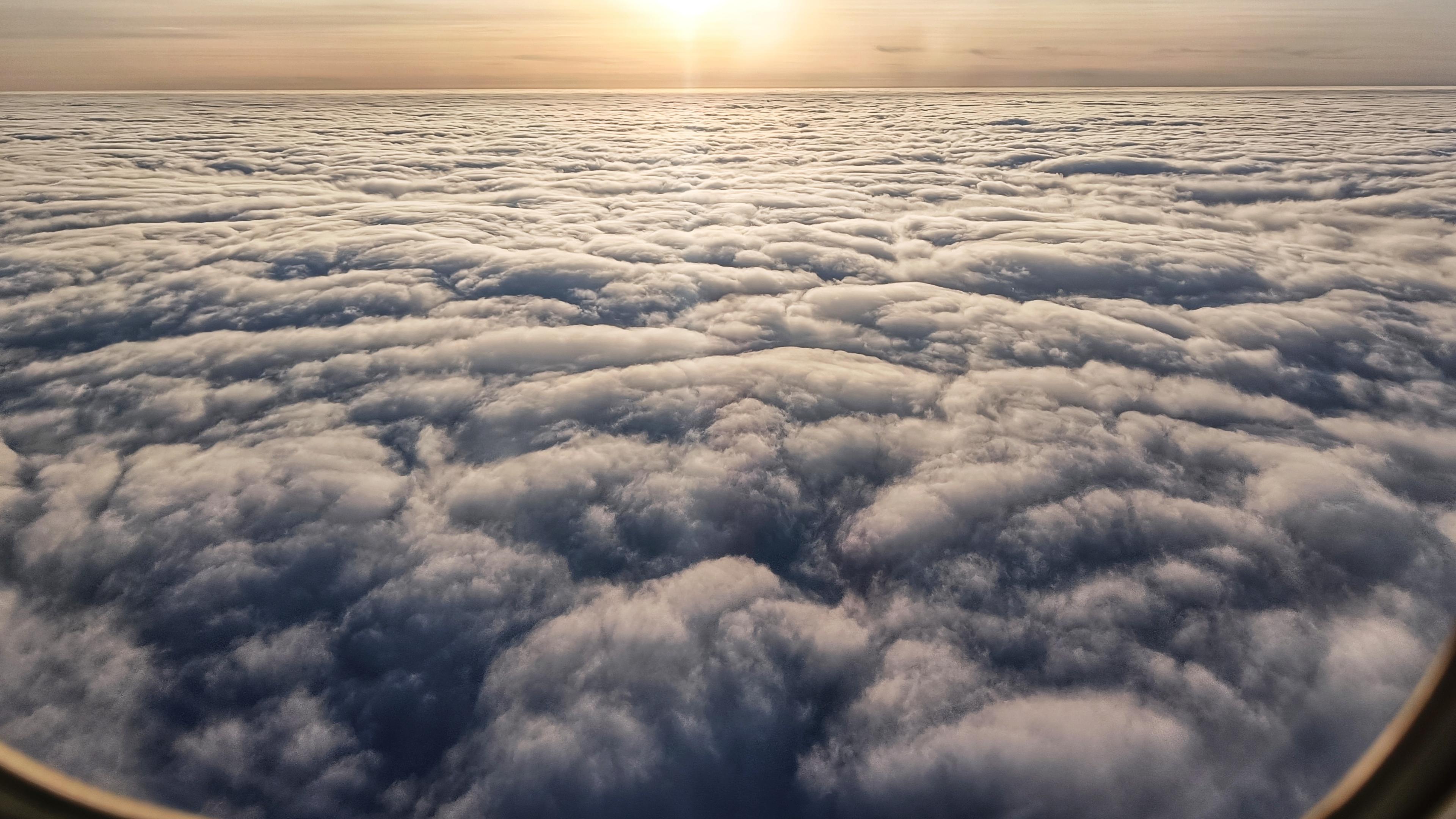 A picture from the window of a plane looking out at a sea of cloud below and the late afternoon sun on the horizon.