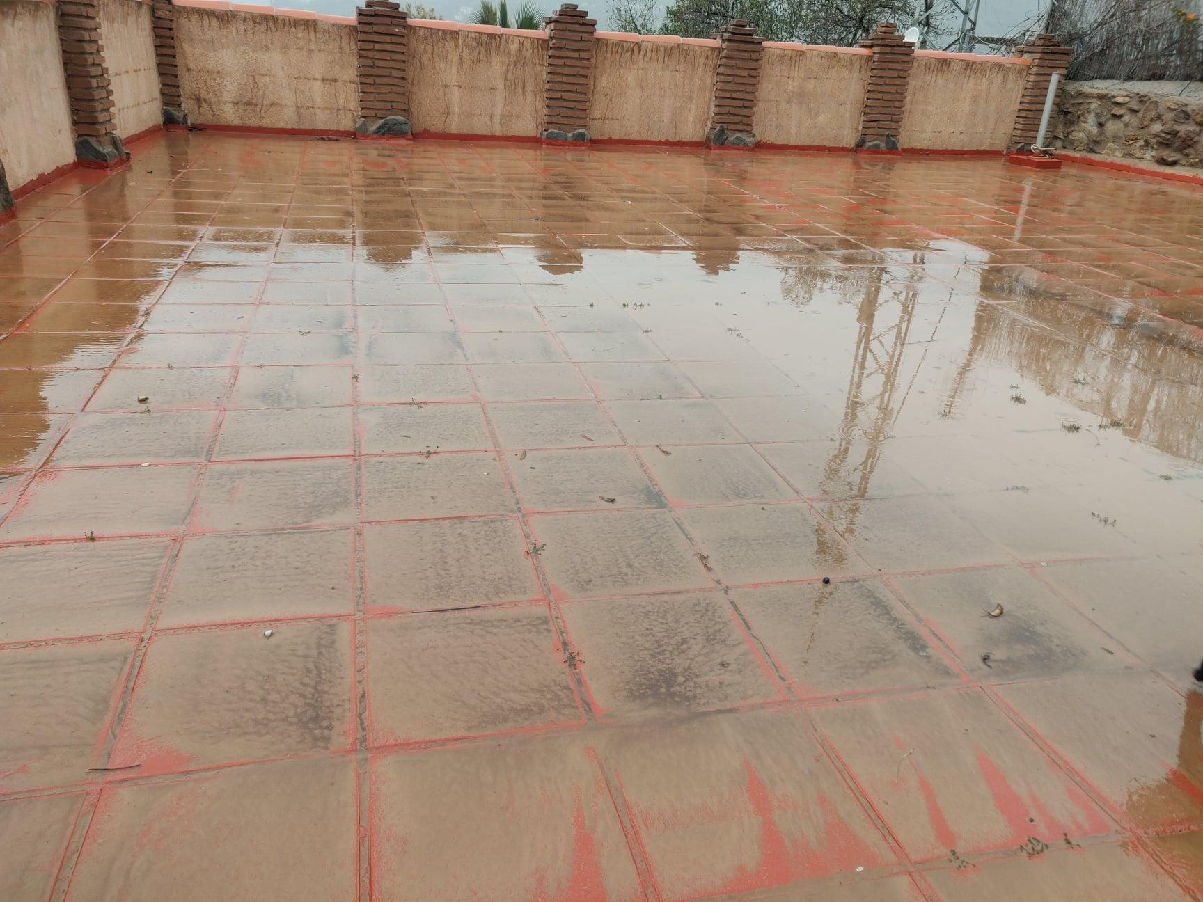 Showing a roof terrace, the once white walls are now mud colour and the red roof is covered in mud