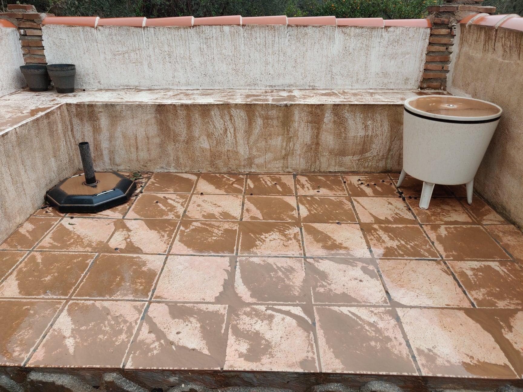 Showing part of a terrace, the white walls and seating area, table and floor are covered in mud.