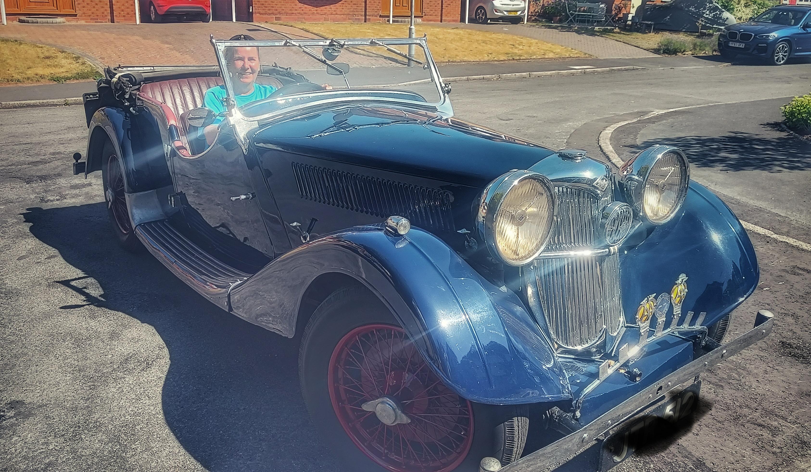 A blue 1938 Riley Lynx car with a person sat in the driver's seat. The car sort of reminds of the one from the film chitty chitty bang bang!